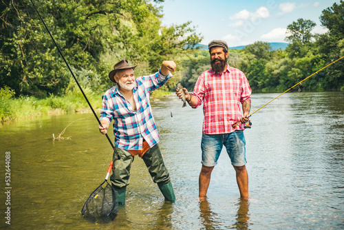 Man friends. Two men friends fishing. Flyfishing angler makes cast, standing in river water. Old and young fisherman.