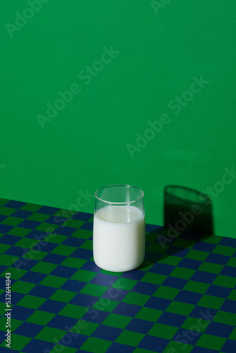 Cup of vegan milk on checkered table against green background photo