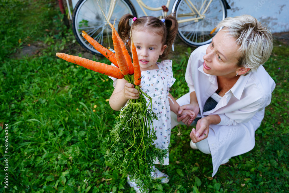 Mom and daughter hold a bunch of carrots near a country house