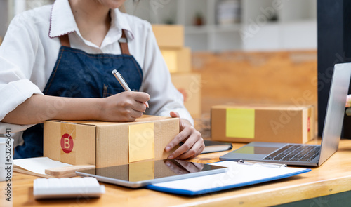 Shipping shopping online, owner writing address on cardboard box at workplace. small business entrepreneur SME or freelance asian woman working with box at home