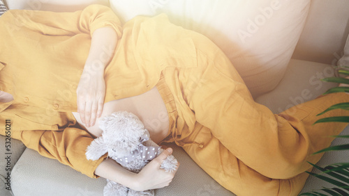 Pregnancy. Young pregnant woman wearing maternity clothes relaxing on home sofa with teddy bear baby toy. Pain of contractions during childbirth. Child expecting. Family planning. Natural pregnancy photo