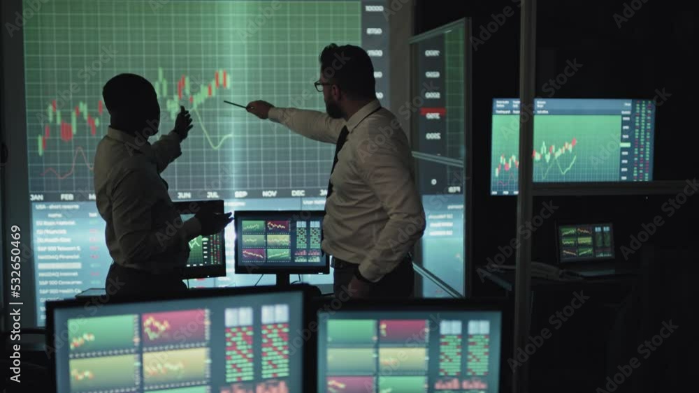 Selective focus of African American and Caucasian men co-working late at night discussing stock trading strategy Selective focus of African American and Caucasian men co-working late at night discussing stock trading strategy