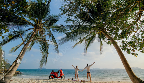 Scooter road trip. Lovely couple on red motorbike in white clothes on sand beach. Just married people kiss hugs walking near the tropical palm trees, sea. Wedding honeymoon by ocean. Motorcycle rent.
