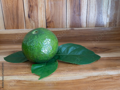 Green avocado fruit and leaves on wooden background.