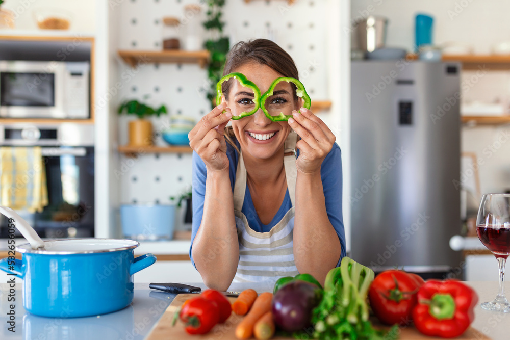 Photo of young woman smiling while cooking salad with fresh vegetables in kitchen interior at home Photo of young woman smiling while cooking salad with fresh vegetables in kitchen interior at home