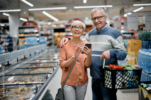 Happy senior couple using app on mobile phone while shopping in supermarket.
