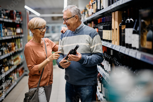 Fotografía Happy senior couple choosing wine while shopping in supermarket.