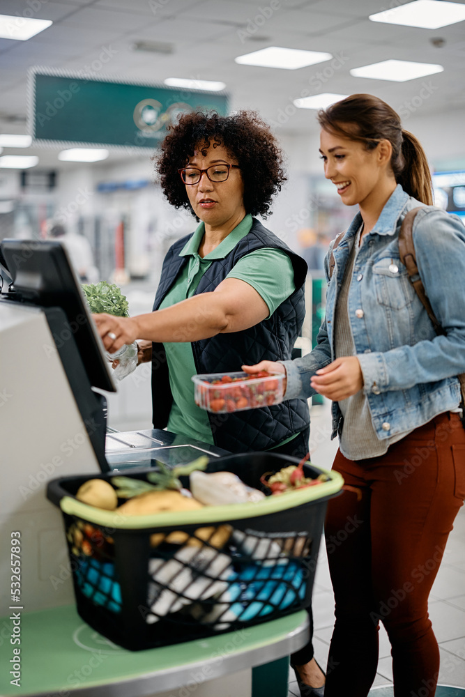 © Drazen - Supermarket worker assists buyer in using self-service till at checkout.