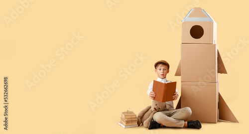 Surprised little boy with books, toy and cardboard rocket on beige background with space for text