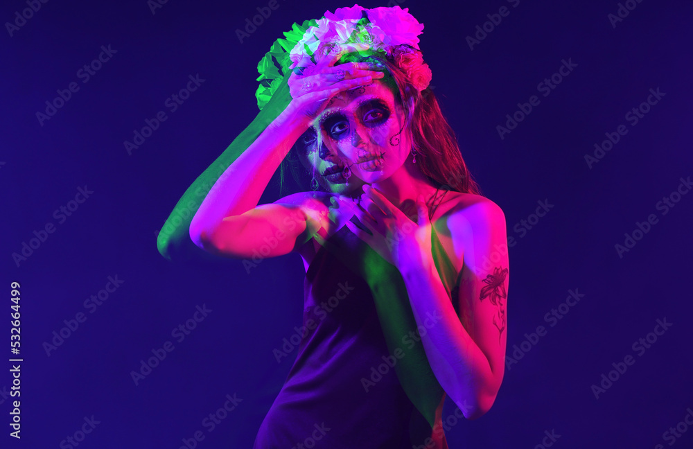Young woman with painted skull on her face for Mexico's Day of the Dead (El Dia de Muertos) against dark blue background