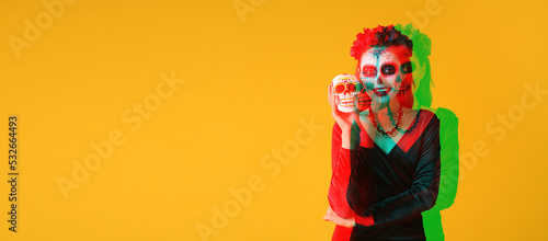 Young woman with painted skull on her face for Mexico's Day of the Dead (El Dia de Muertos) against yellow background with space for text © Pixel-Shot