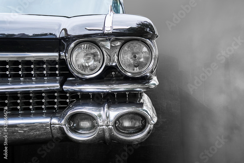 Front headlights of antique American road cruiser against blurred background, monochrome image