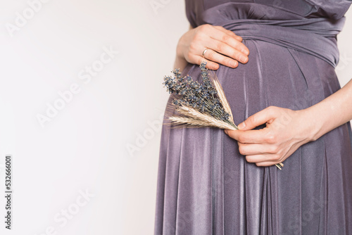 Pregnant woman in violet dress touching belly, preparing go to maternity hospital for childbirth. Pregnancy, maternity, preparation, baby expectation concept. 40 weeks of pregnancy. White background