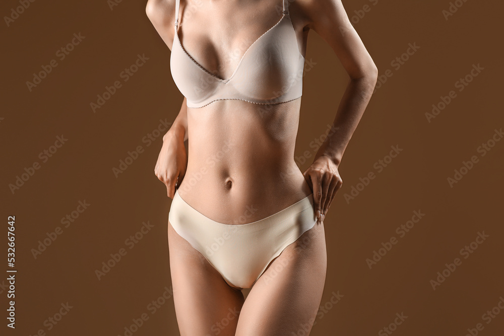 Slim young woman in underwear on brown background
