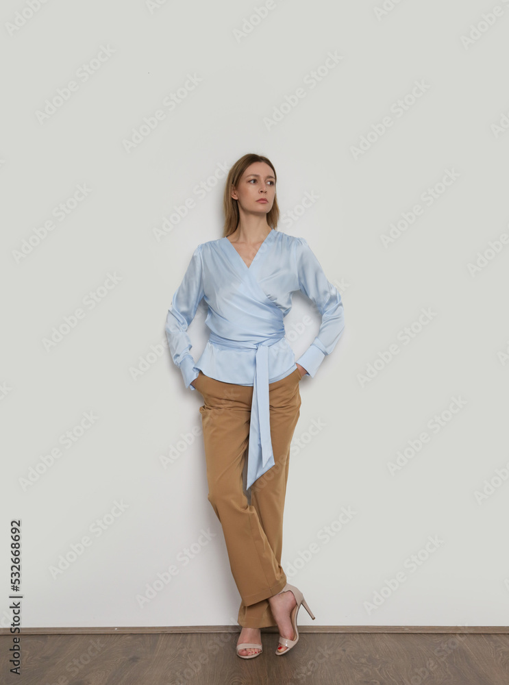 Serie of studio photos of young female model wearing simple beautiful outfit, silk satin wrap blouse and straight leg trousers Serie of studio photos of young female model wearing simple beautiful outfit, silk satin wrap blouse and straight leg trousers