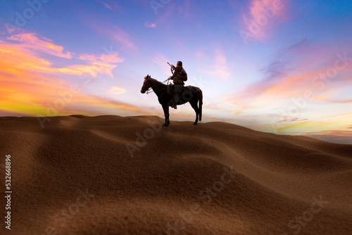 silhouette cowboy ride horse with holding rifle on hand on dessert with twilight sky background.
