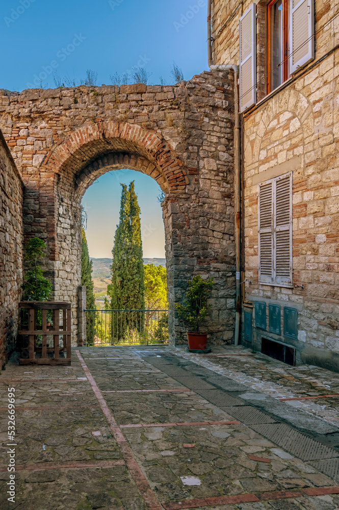 An arch in the ancient walls of Todi, Perugia, Italy, with a cypress in the background