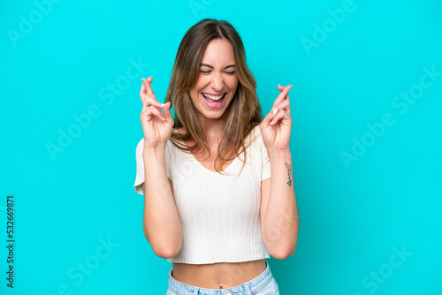 Young caucasian woman isolated on blue background with fingers crossing
