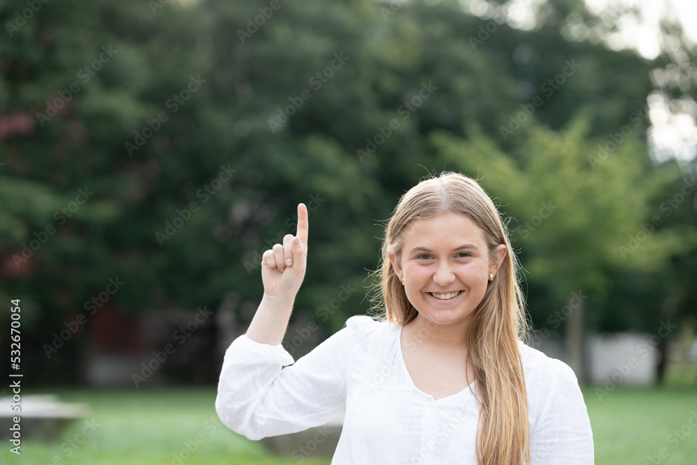 Beautiful chubby teenager girl pointing up to copy space outdoors in a park. Beautiful chubby teenager girl pointing up to copy space outdoors in a park.