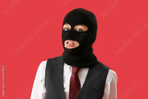 Young woman in balaclava with burning match in mouth on red background