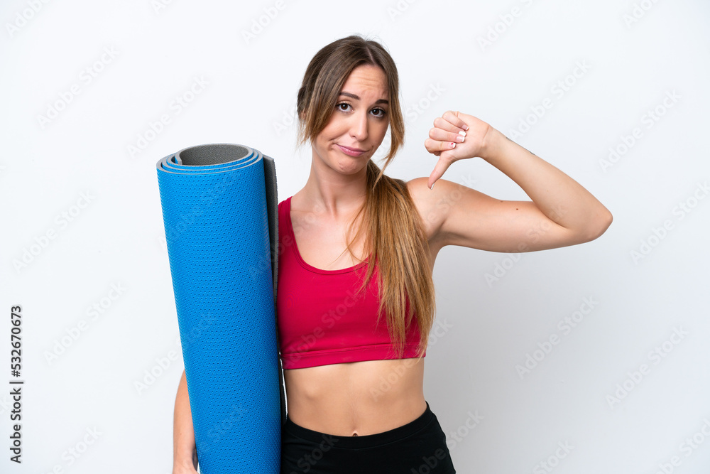Young sport woman going to yoga classes while holding a mat isolated on white background showing thumb down with negative expression