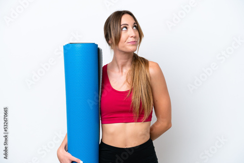Young sport woman going to yoga classes while holding a mat isolated on white background and looking up