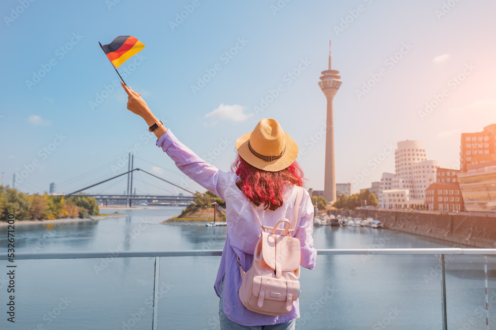 A young happy Asian girl with a German flag poses at the Media Harbor and TV-tower in Dusseldorf. Studying language abroad and traveling concept