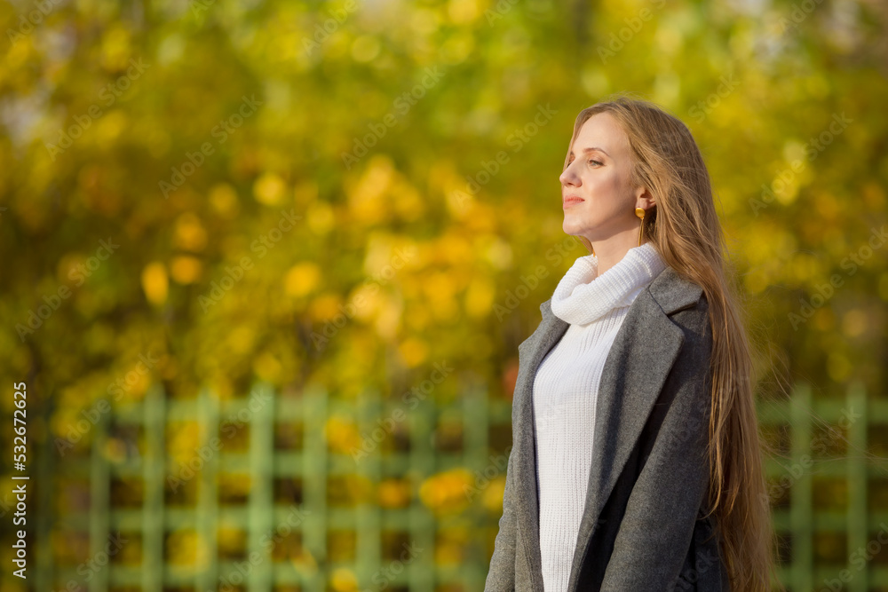 Young woman walks in the autumn park. Portrait of a beautiful woman in an elegant gray coat and white sweater. Pretty woman with light brown hair on a background of yellow foliage. Fall season. Young woman walks in the autumn park. Portrait of a beautiful woman in an elegant gray coat and white sweater. Pretty woman with light brown hair on a background of yellow foliage. Fall season.