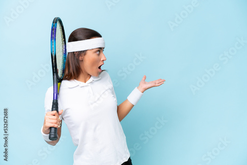 Young tennis player woman isolated on blue background with surprise expression while looking side