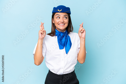 Airplane stewardess caucasian woman isolated on blue background with fingers crossing