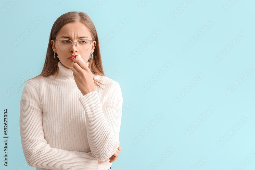 Young woman with nosebleed and tissue on blue background Young woman with nosebleed and tissue on blue background