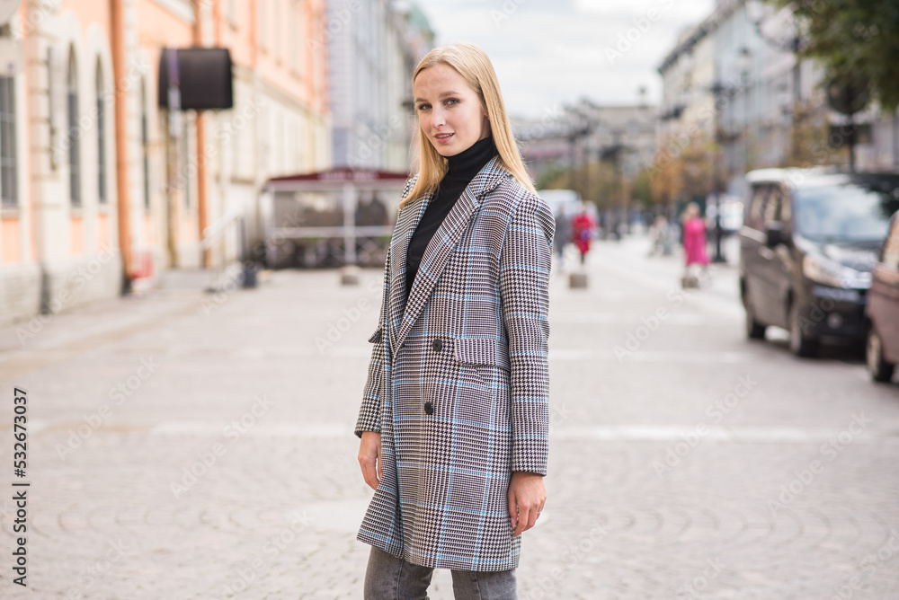Portrait of a young and elegant Caucasian blonde girl in autumn in the city. The concept of femininity and style. A pretty girl is happy to pose in the city on the street in a coat.