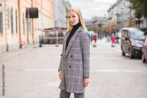 Portrait of a young and elegant Caucasian blonde girl in autumn in the city. The concept of femininity and style. A pretty girl is happy to pose in the city on the street in a coat.