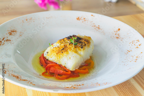 Delicious baked cod with roasted red pepper on wooden table.