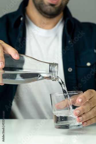Unrecognizable man pouring water into a glass to hydrate himself - hydration and wellness concept