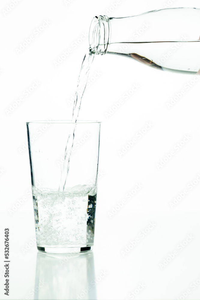 Detail of a glass bottle pouring water into a glass tumbler on a white background. Detail of a glass bottle pouring water into a glass tumbler on a white background.
