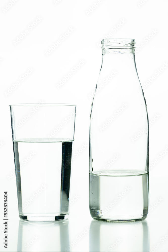 Glass tumbler and glass bottle in foreground filled with water on white background Glass tumbler and glass bottle in foreground filled with water on white background