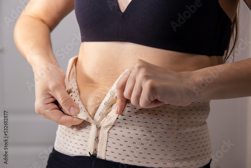 Closeup woman getting dressed, hooking on corset hooks using hands behind back, weightloss concept. A woman fastens a corset for figure correction.