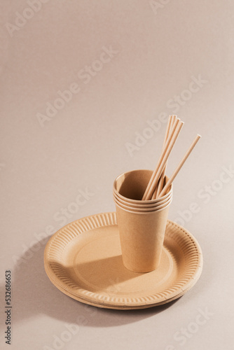 Disposable paper tableware. Cups, plates and straws on beige background. Plastic free and zero waste concept.