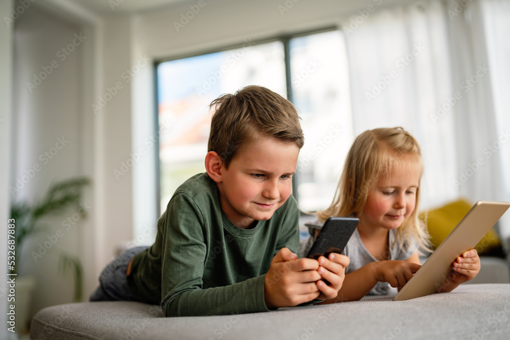 Fototapeta premium Little girl and boy watching video or playing games on their digital device tablet, smartphone.