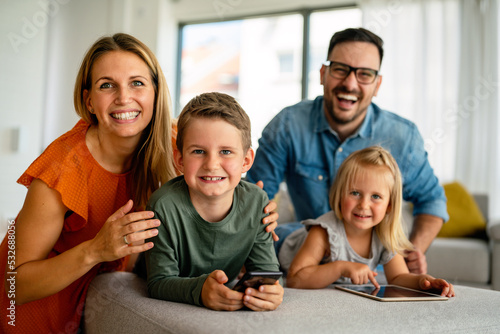 Happy young family having fun time at home. Parents with children using digital device.