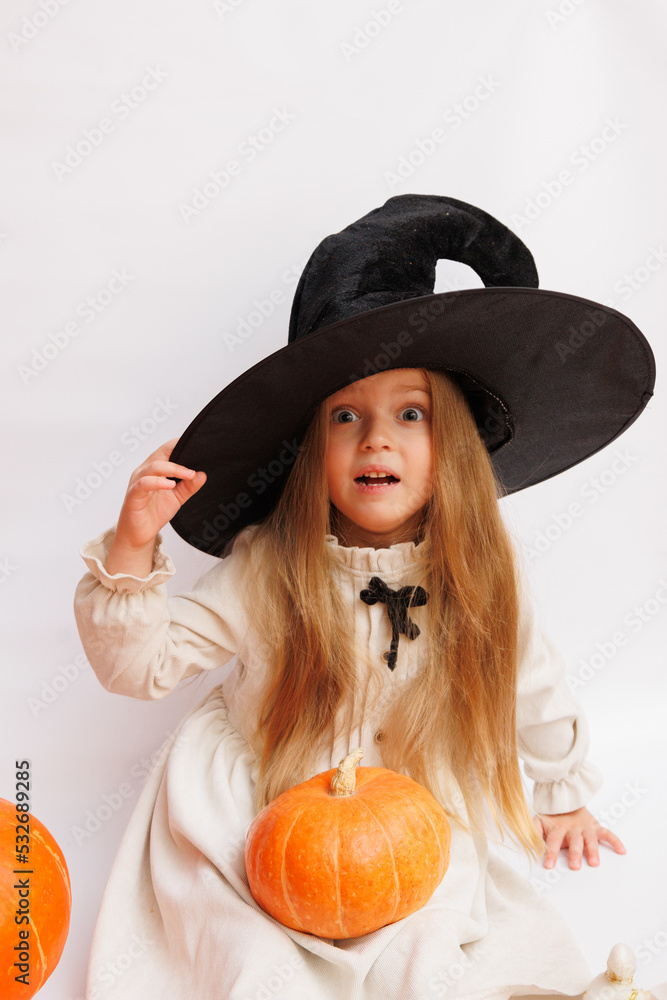 Halloween portrait of a little girl in a witch magic hat. Little child with pumpkins. White background. Halloween portrait of a little girl in a witch magic hat. Little child with pumpkins. White background.