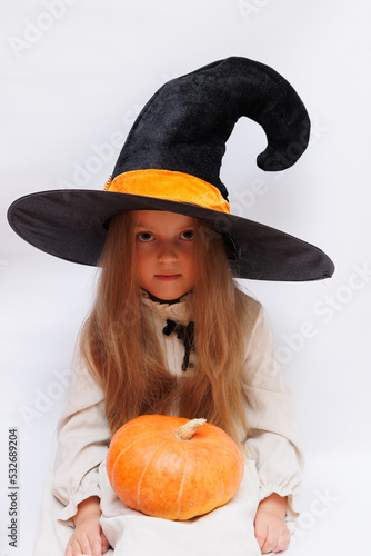 Halloween portrait of a little girl in a witch magic hat. Little child with pumpkins. White background.  photo