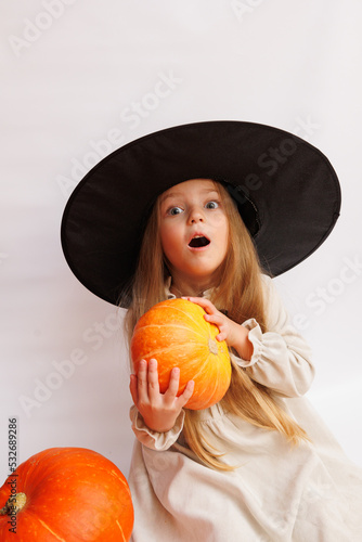 Halloween portrait of a little girl in a witch magic hat. Little child with pumpkins. White background.  photo