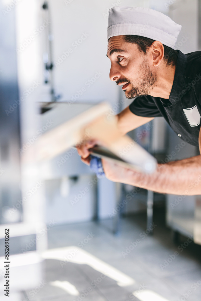 Italian chef pizzaiolo putting pizza to oven in restaurant kitchen Italian chef pizzaiolo putting pizza to oven in restaurant kitchen