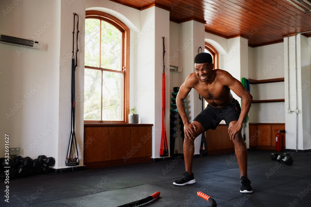 Determined young black man doing squats by battle ropes at the gym Determined young black man doing squats by battle ropes at the gym