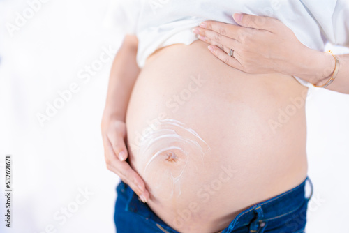 カジュアルな服装で妊娠線予防クリームを塗る妊婦 斜め（本物の臨月妊婦さんを撮影）