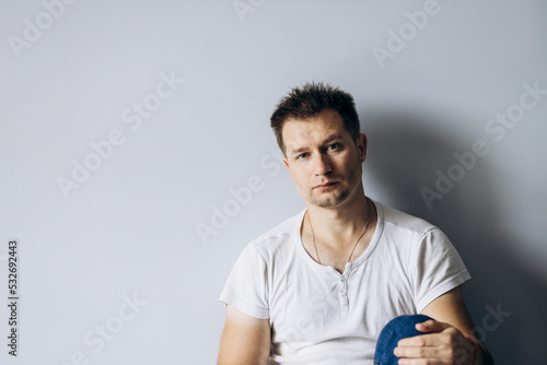 Handsome man in white t-shirt sits on floor thoughtfully sad.