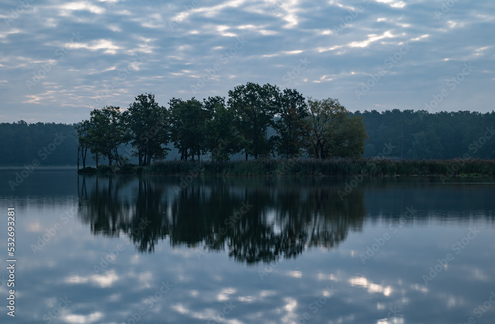 Reflections in the water of a small island covered with trees Reflections in the water of a small island covered with trees
