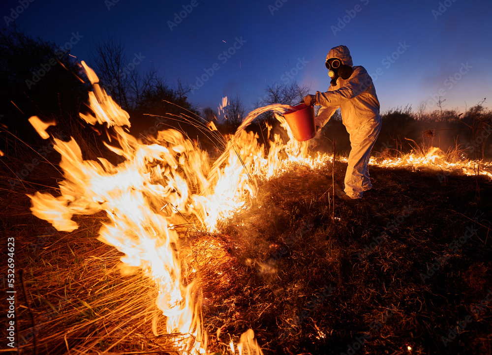 Fireman extinguishing fire in field with blue night sky on